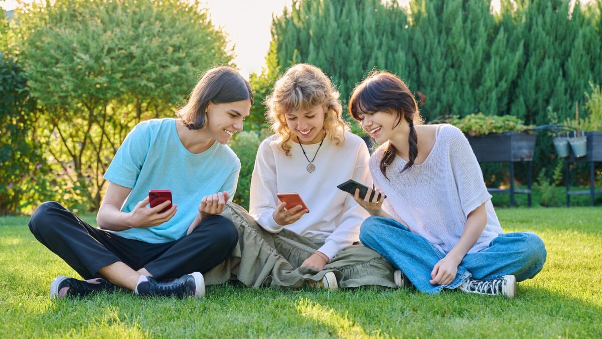 Teenage friends sitting on the grass with smartphones