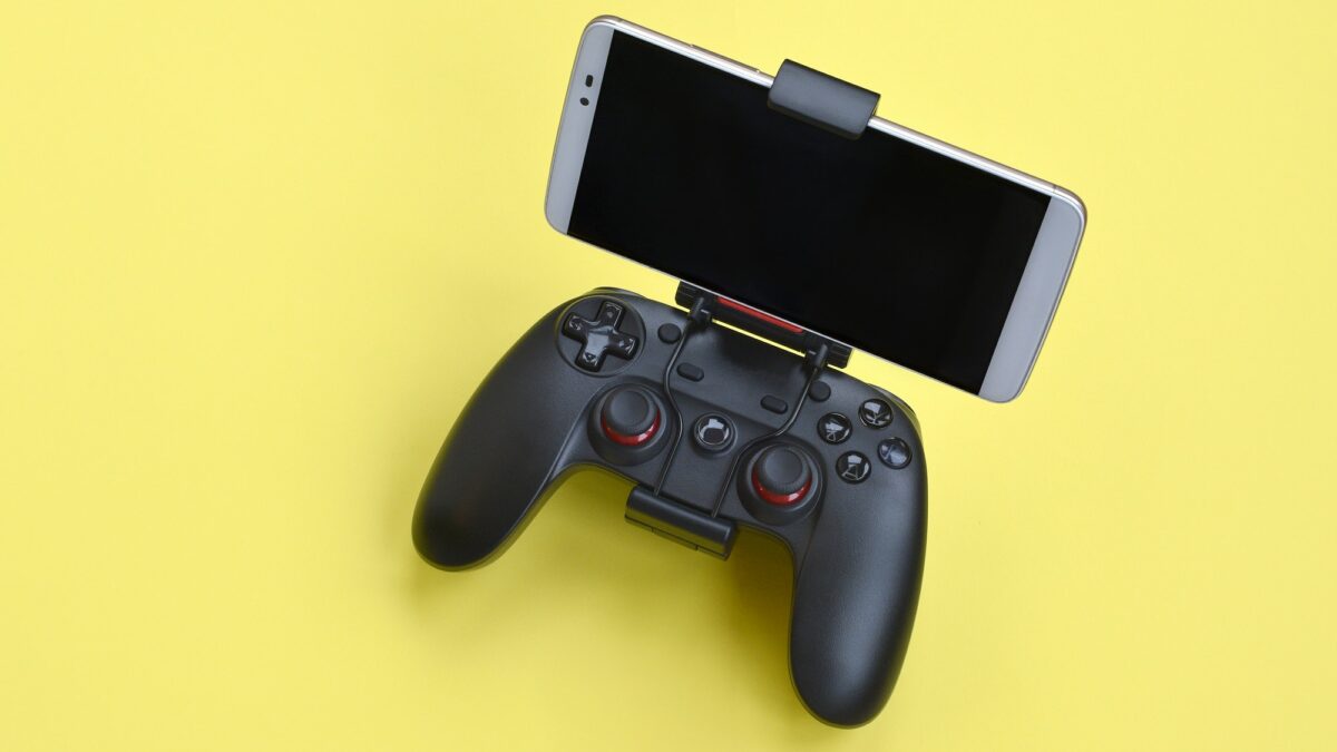 Modern black gamepad for smartphone on yellow background close up. Mobile video gaming device