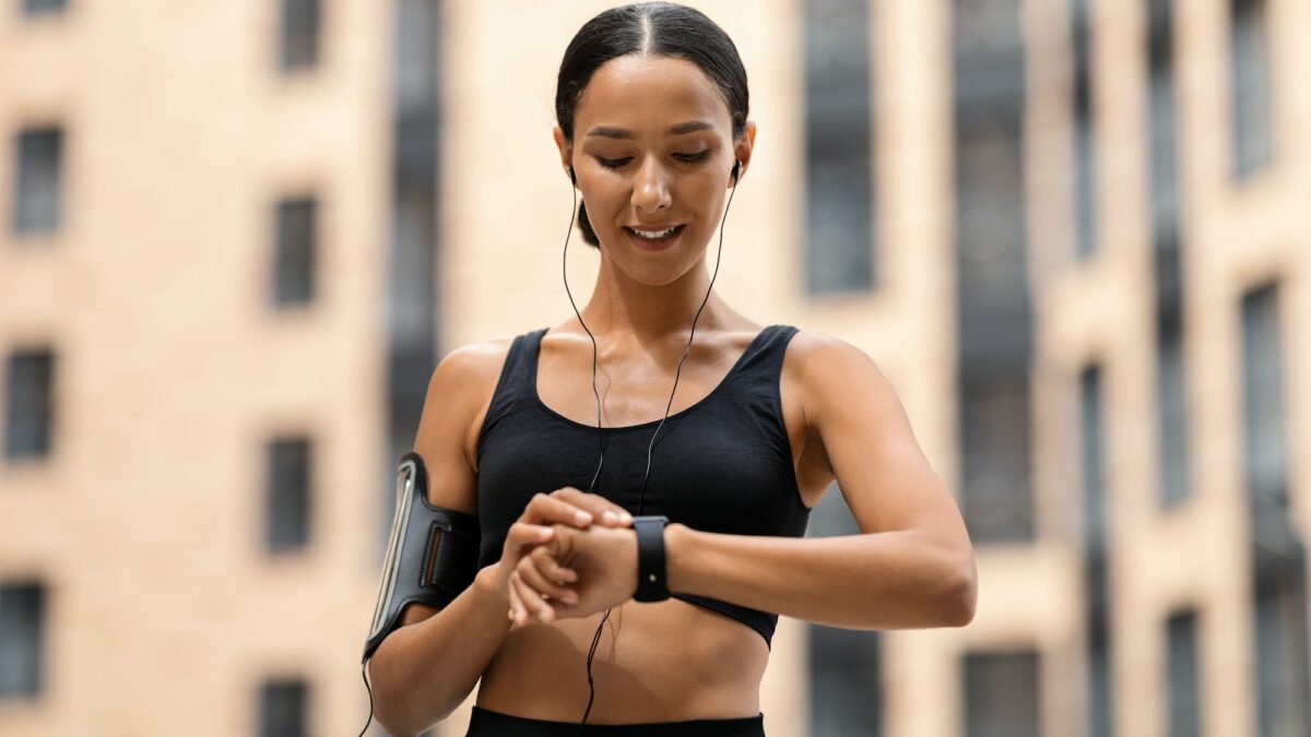 Sporty Young Woman Looking At Smartwatch, Tracking Fitness Activity During Training Outdoors