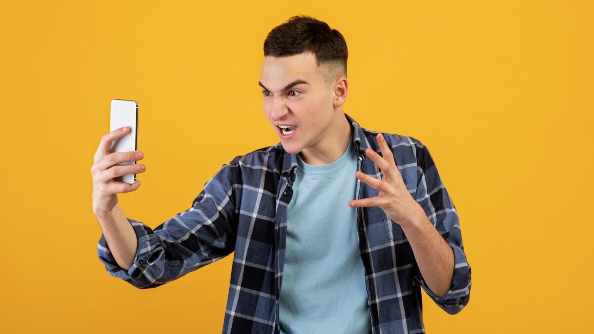 Wütender Mann, der auf sein Smartphone schaut, orangener Hintergrund