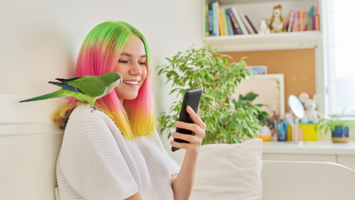 Trendy teen girl with smartphone and quaker parrot on her shoulder