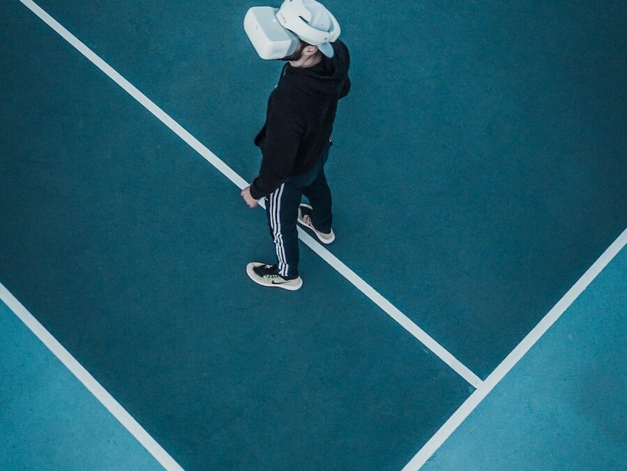 man in track suit wearing VR headset standing on tennis court