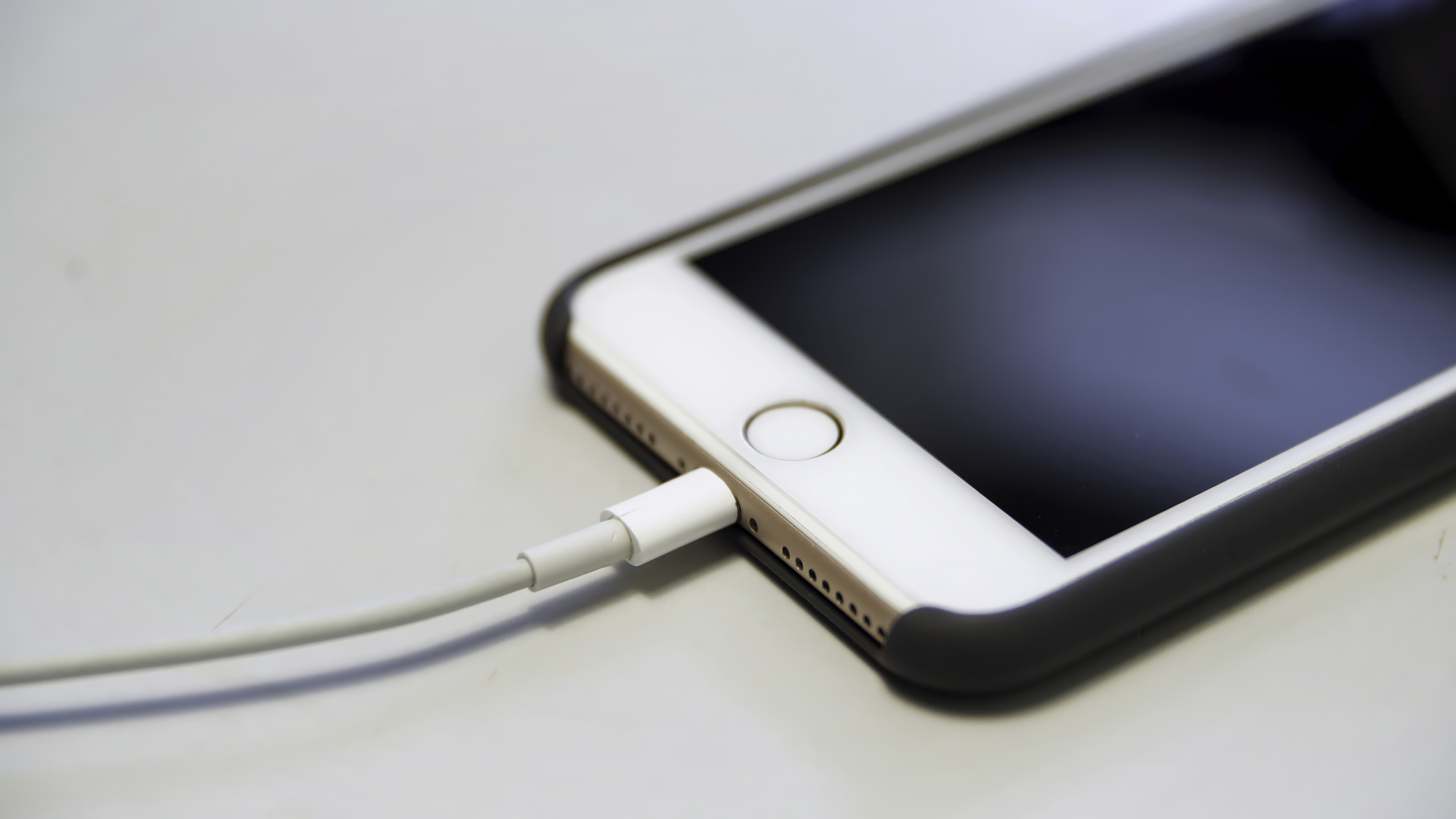 Close up of the apple iphone with the charging cable lying on the white table. Media. Process of