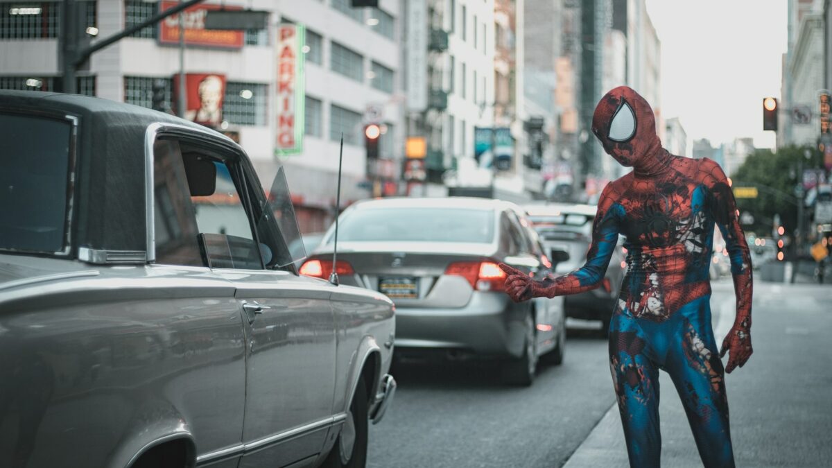man wearing Spider-Man costume standing on sidewalk with cars on roadway