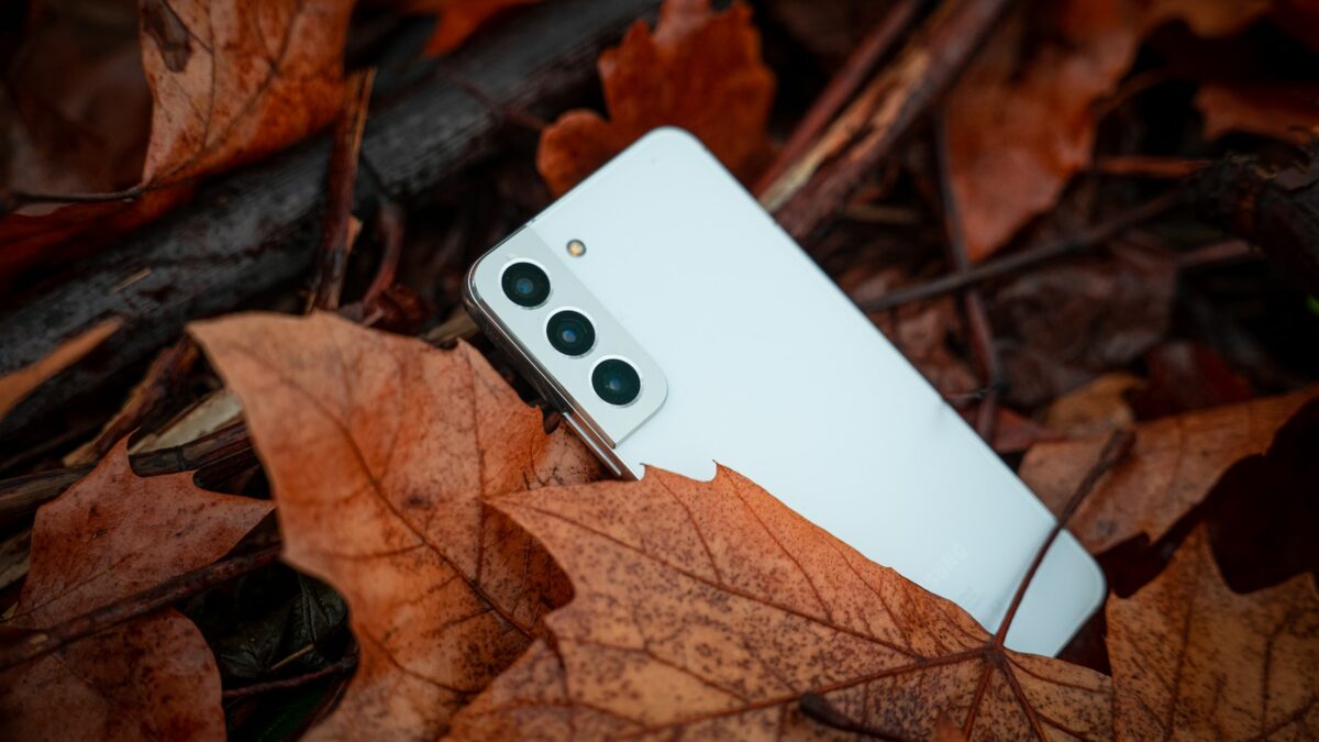 a white cell phone laying on top of a pile of leaves