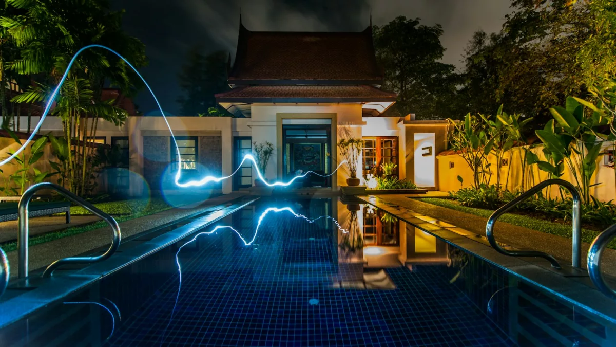 reflection of blue light crossing above pool near house during nighttime